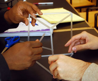 Two pairs of hands hold a tower made of straws.