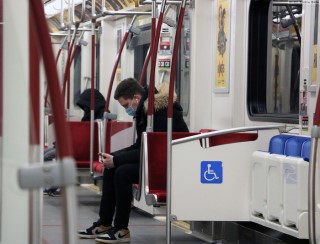 A man sits in a nearly-empty subway car, wearing a face mask.