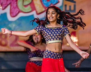 A young, brown-skinned girl with a smiling face dances, her long hair in motion.