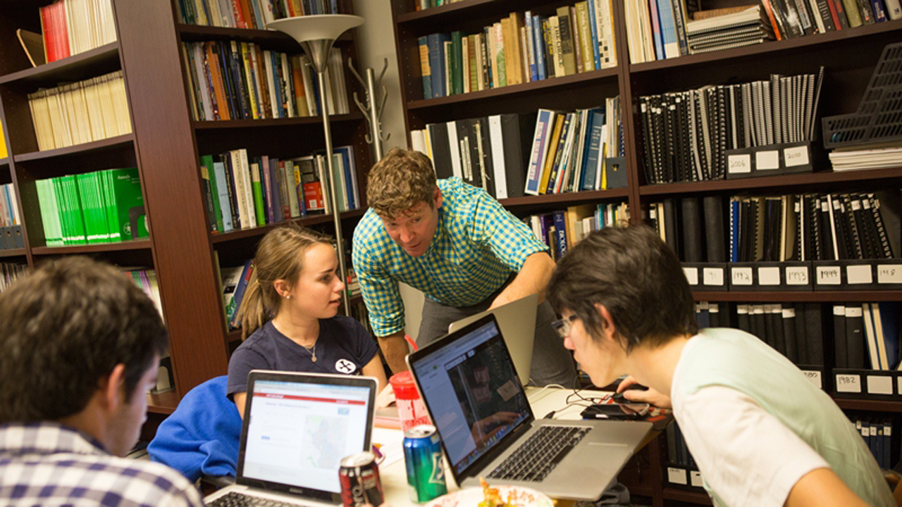 four college students working on their laptops at a desk in the library